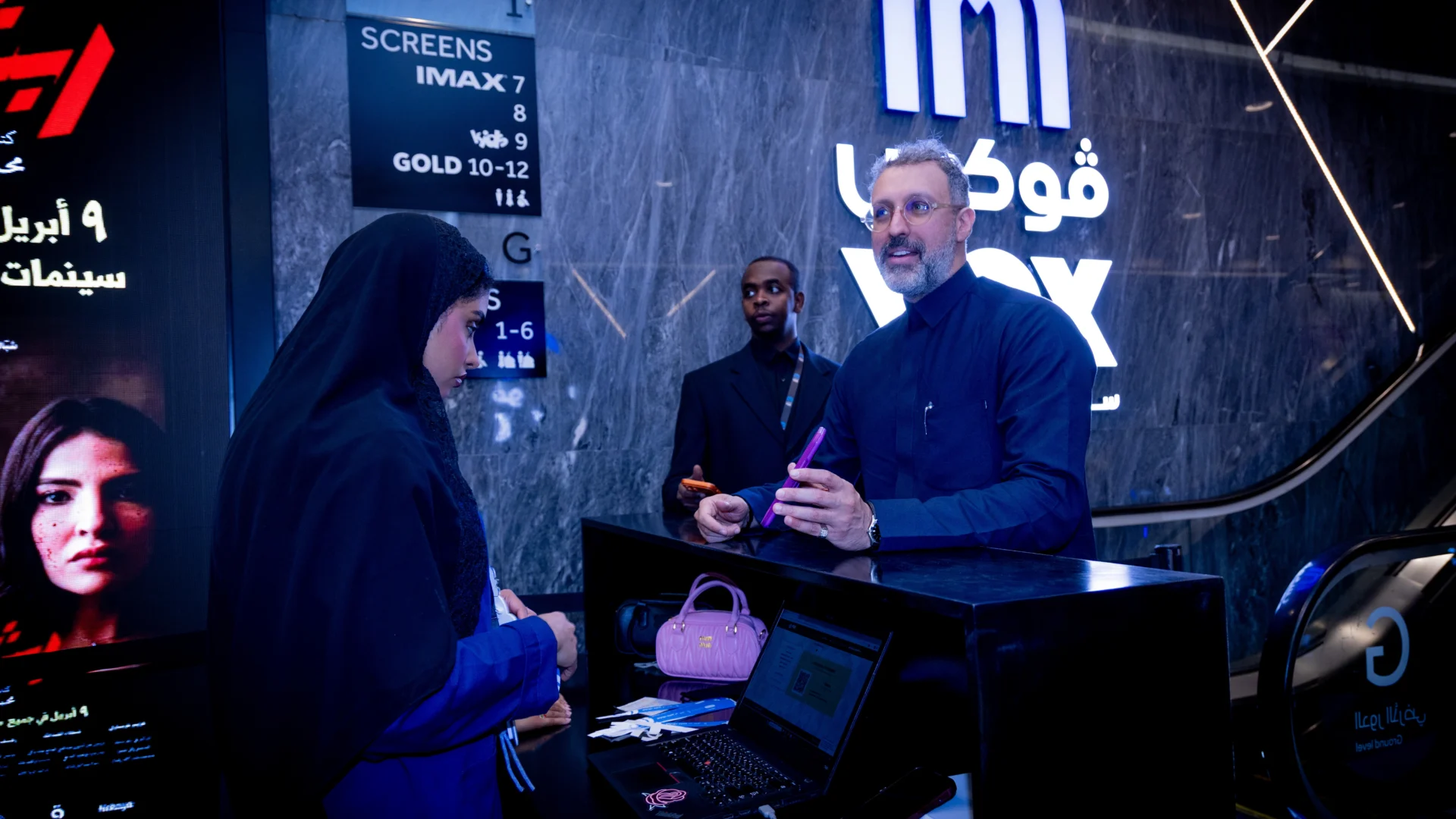 Event coverage of the check-in reception desk at the Rabsha film premiere night, showing guests arriving and staff assisting at the counter.